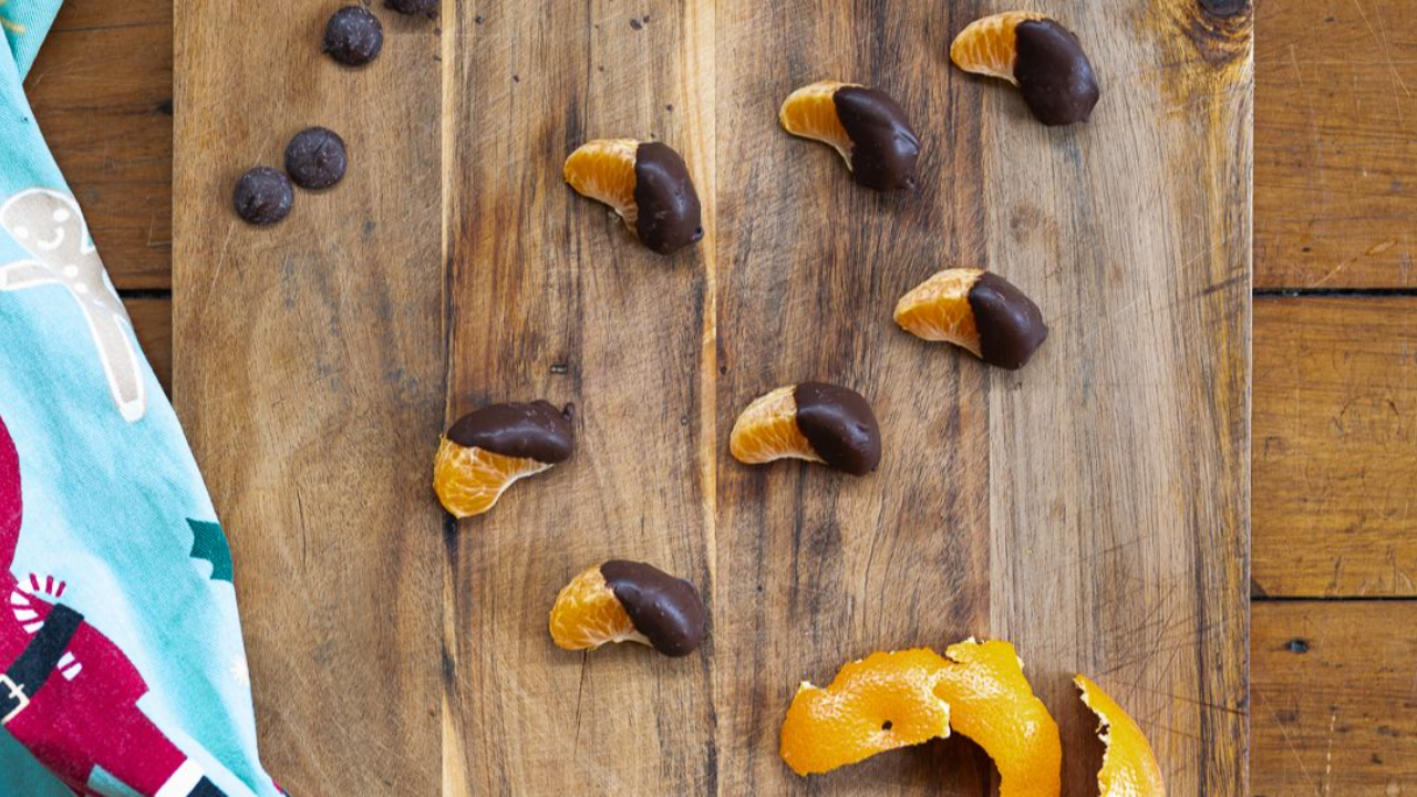 fresh orange segments half dipped in dark chocolate arranged on board
