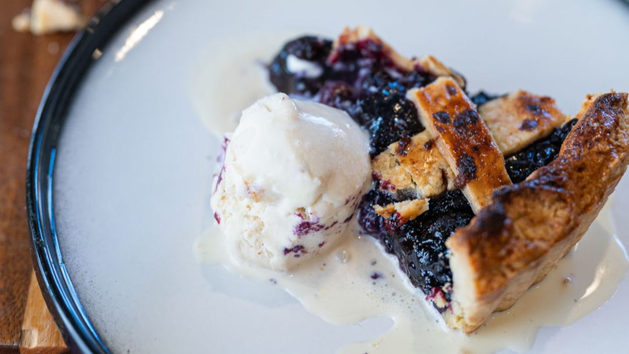 blueberry pie with golden lattice pastry top showing purple berry filling baked until bubbling with ice cream