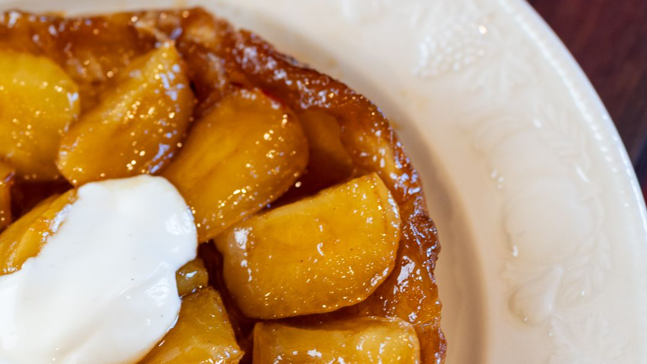 golden apple tarte tatin with caramel and puff pastry turned out onto a plate with a dollop of cream
