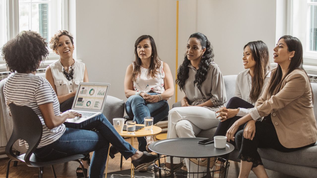 group of women gathered together for meeting, one has a computer with stats