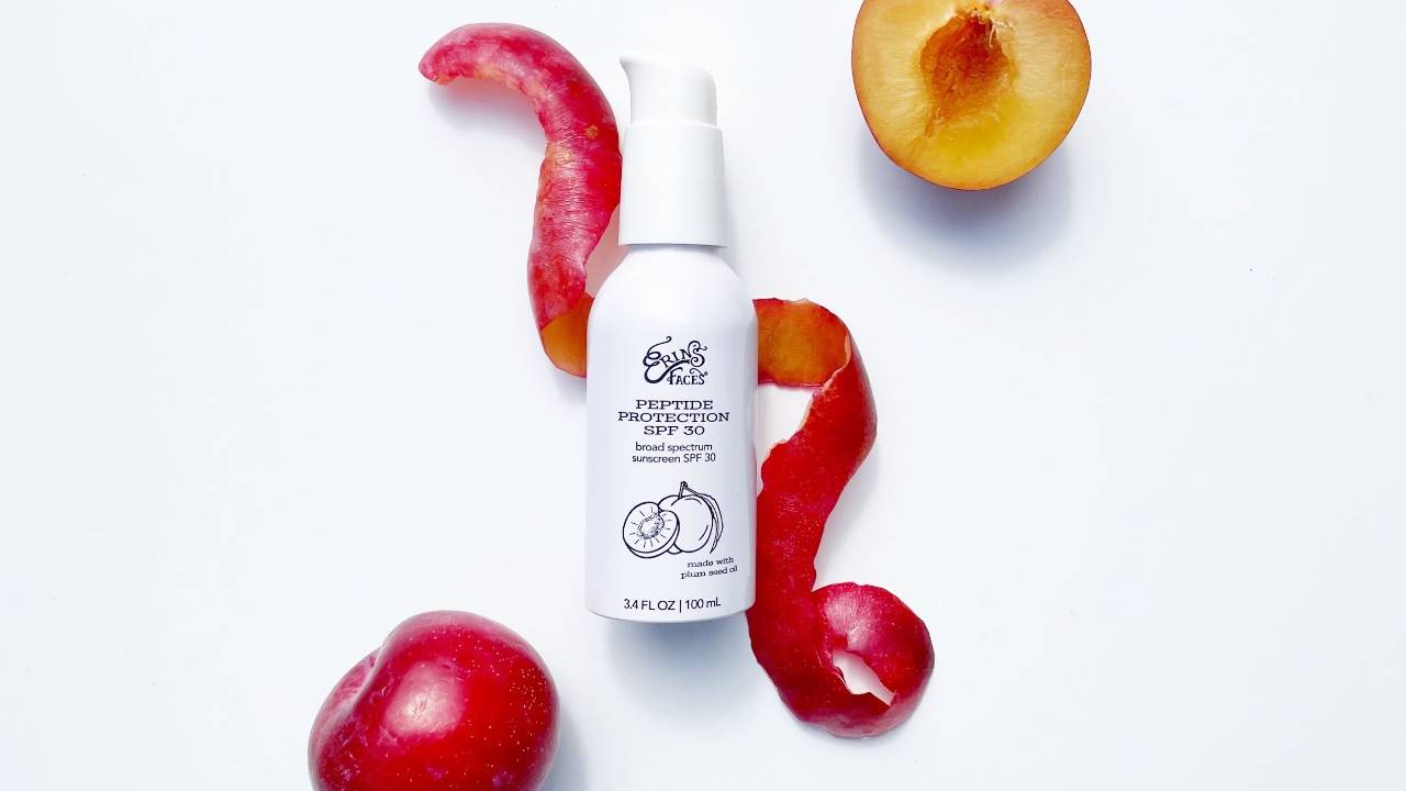 white background, plum shown with plum peel spiral topped by a white aluminum bottle of erin's faces peptide protection spf 30