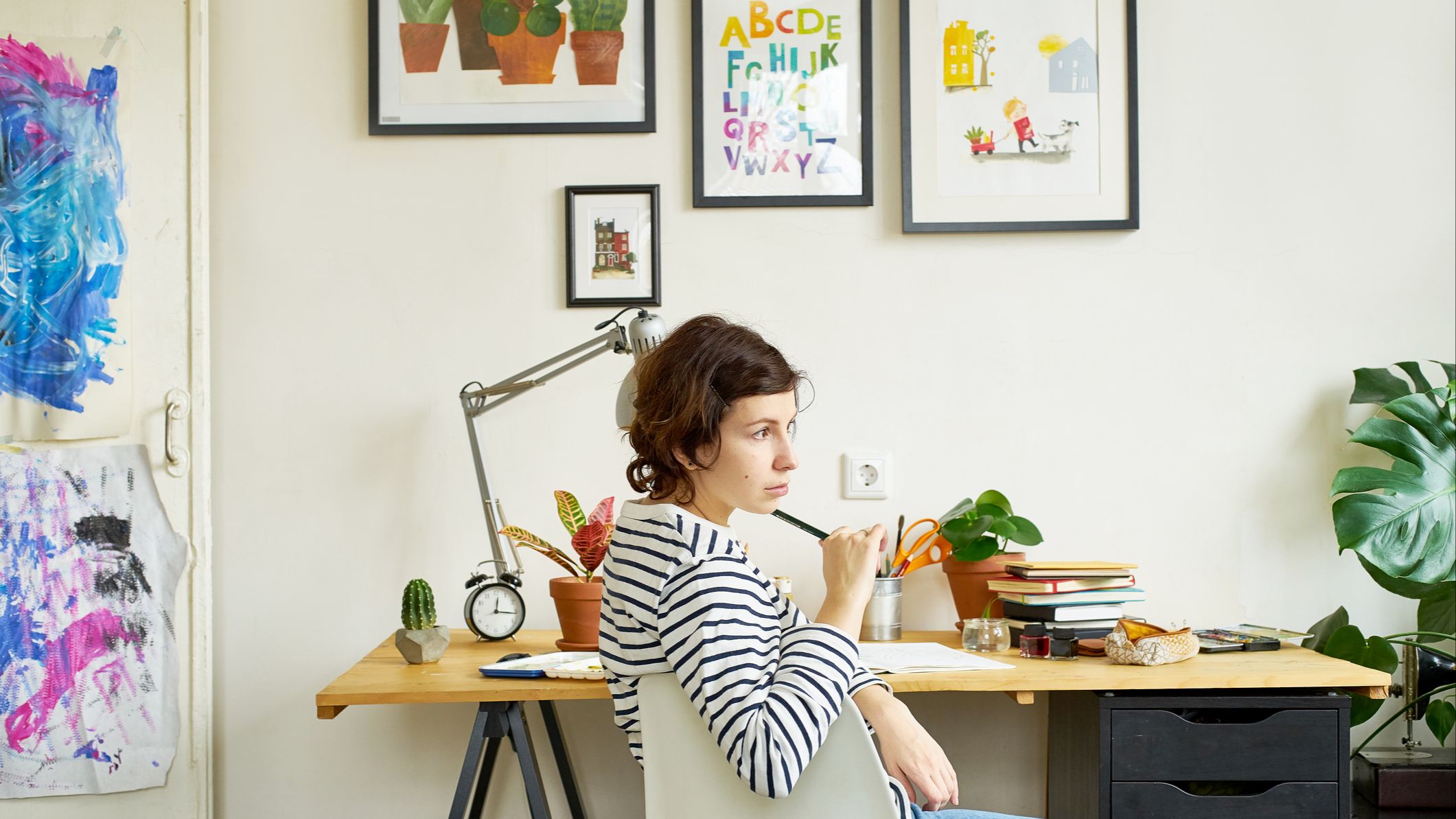 Female artist at her workplace working from home. Young woman dressed in jeans and striped shirt sitting at the table and thinking.