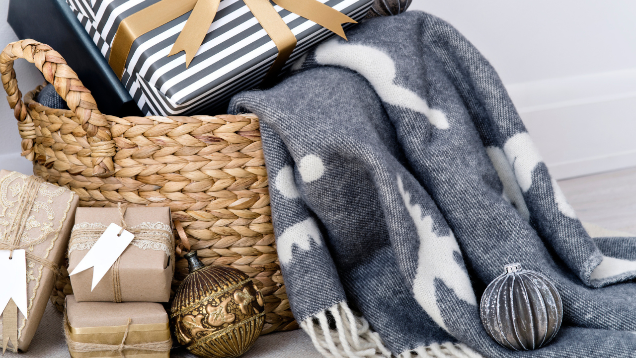 Composition of stylish gift boxes with blank tags and vintage glittering Christmas balls. Charming wrapped gifts and woven blanket in a basket.