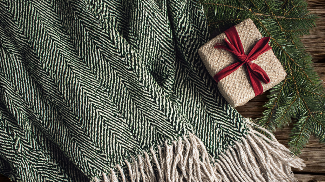 Green herringbone woven throw blanket with small wrapped gift and pine branch.