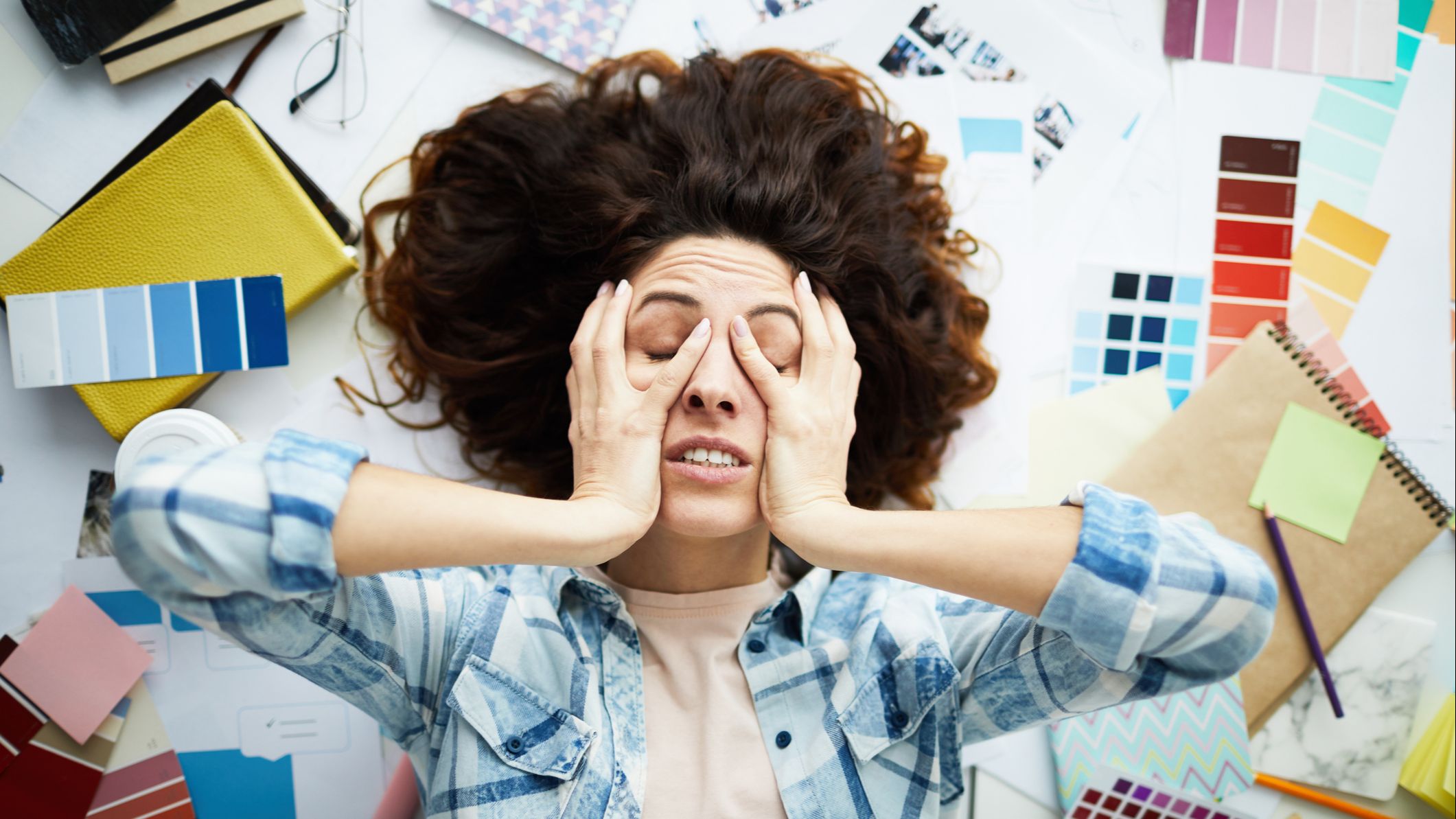 Top view portrait of exhausted designer lying in pile of work with eyes closed.