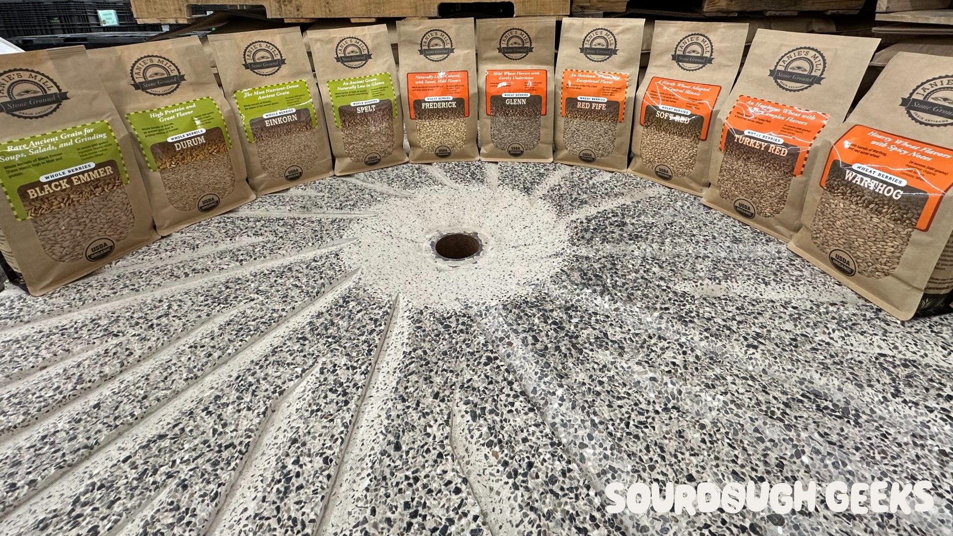 Bags of different artisan baking flours arranged in an arc on a stone mill