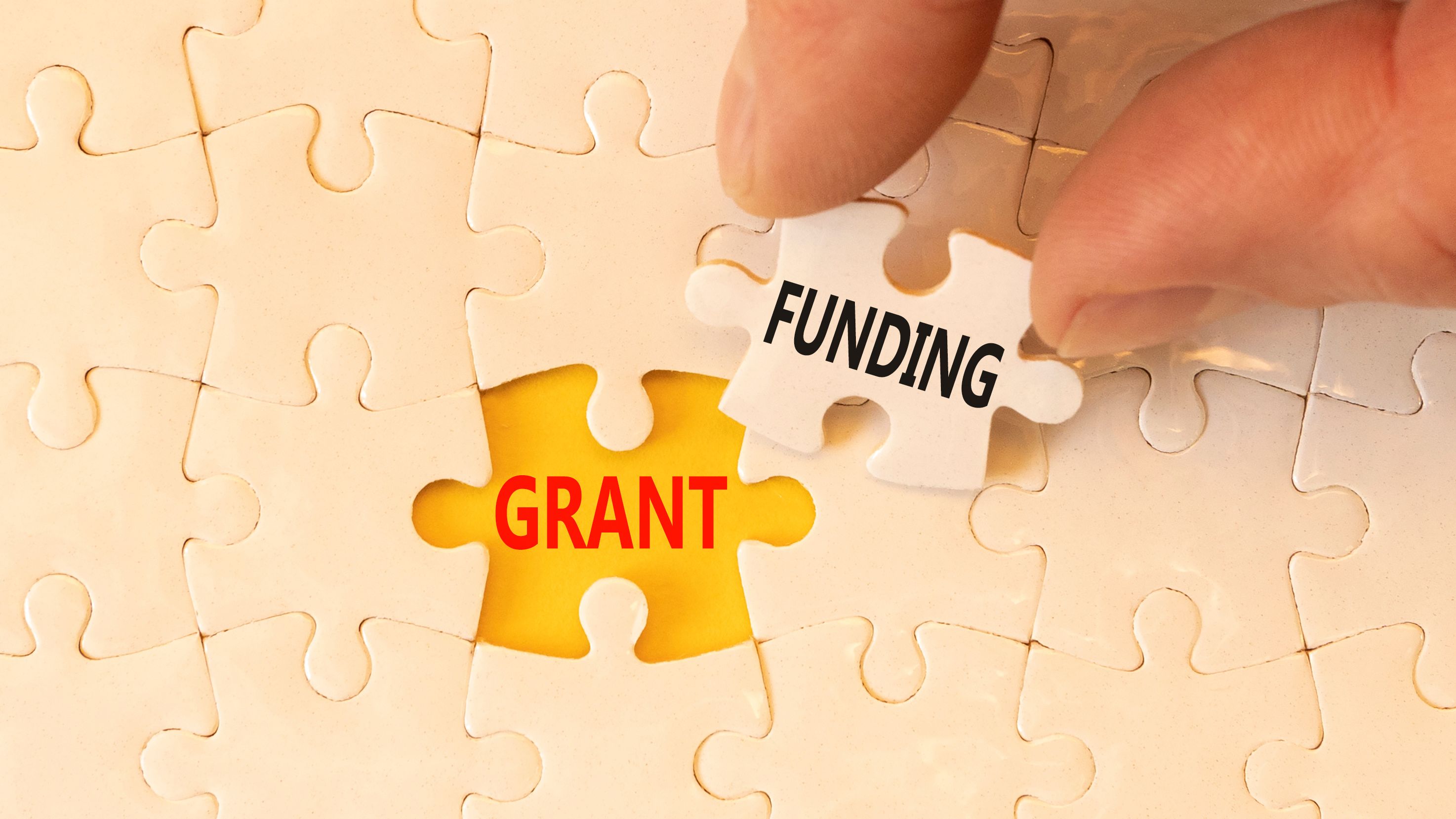 Hand placing puzzle piece labeled 'funding' next to 'grant,' symbolizing the steps to request additional nonprofit funding after a grant award, essential for completing project funding.