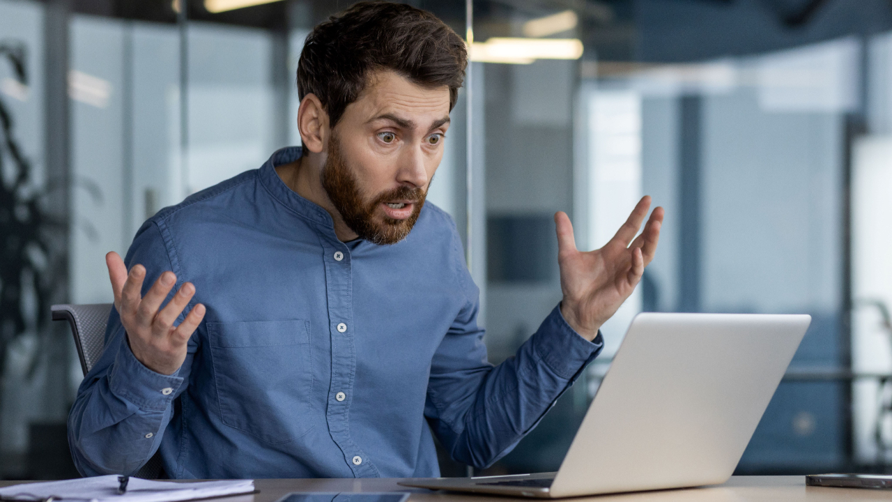 A surprised grant writer reacting to a document on their laptop, reviewing outcomes and outputs for a successful grant application.