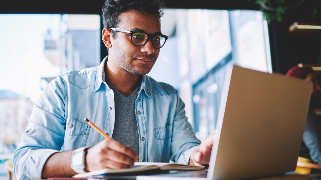 Man writing a grant proposal on laptop, highlighting the importance of outputs, outcomes, and impacts in grant writing.