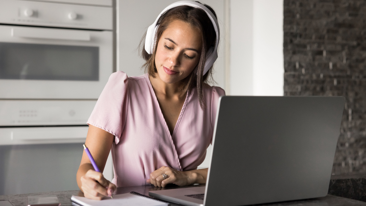 Focused woman, taking notes while working on a laptop, illustrating the process of writing a project description for a grant application, emphasizing clarity, alignment, and impact.