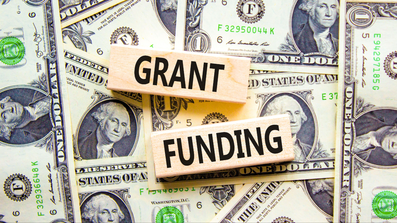 Blocks labeled 'Grant Funding' placed over a background of dollar bills, symbolizing financial planning and budgeting for grant applications.