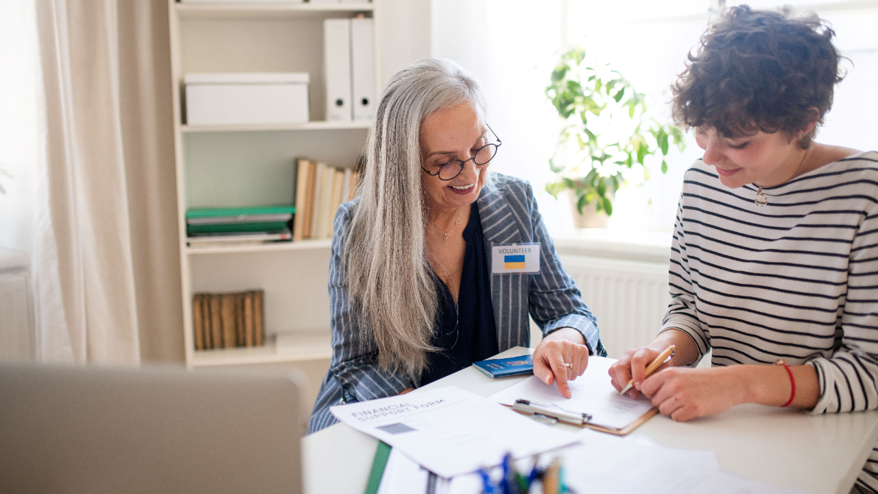 An experienced volunteer helping a young woman complete a grant application, focusing on accurately describing project beneficiaries to improve funding success.