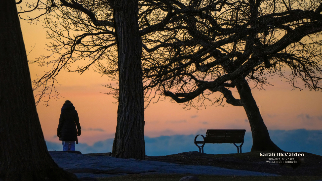 Woman walking through trees near a bench in the winter at sunset