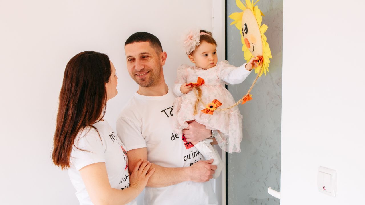 Mama și tata jucându-se împreună cu copilul în camera de zi, zâmbind și interacționând afectiv.