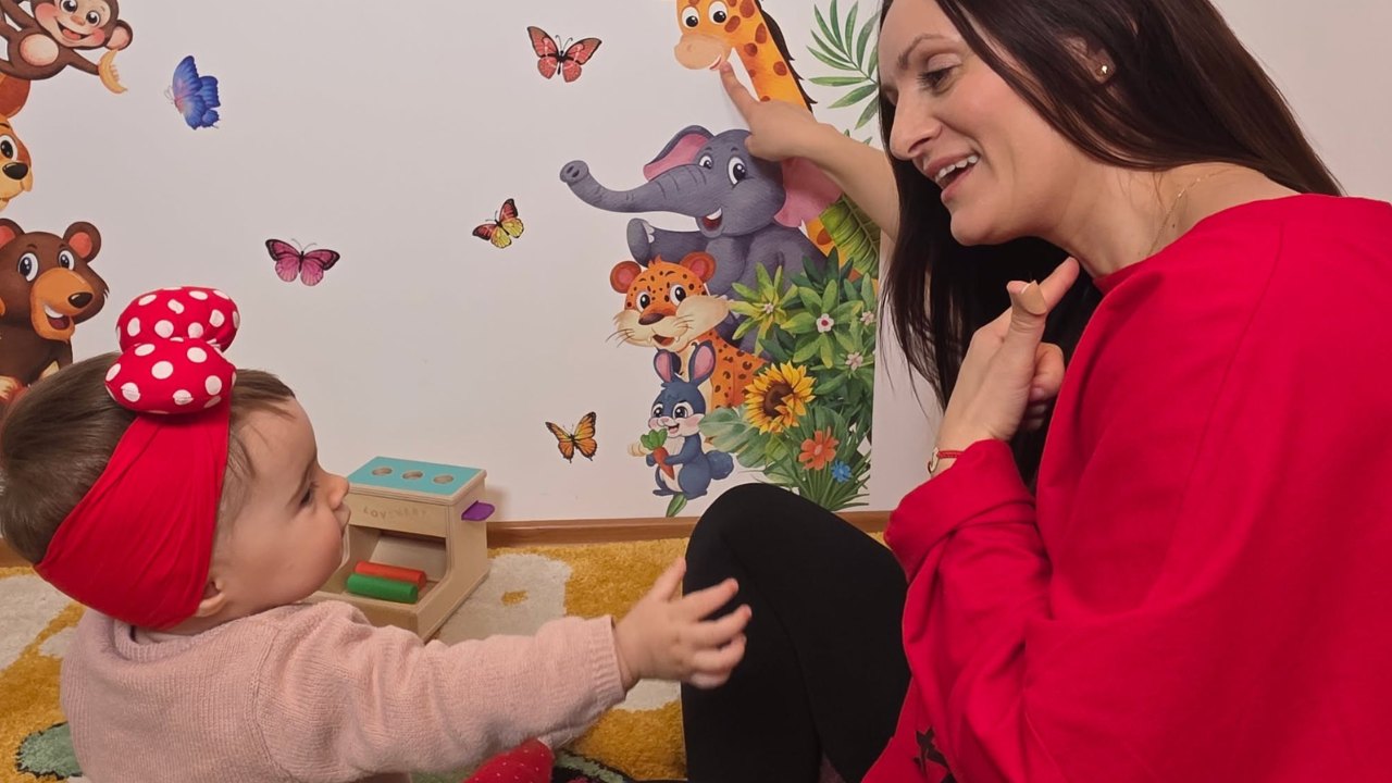 Mamă zâmbitoare care citește o carte împreună cu fetița ei mică, în camera luminoasă și primitoare.