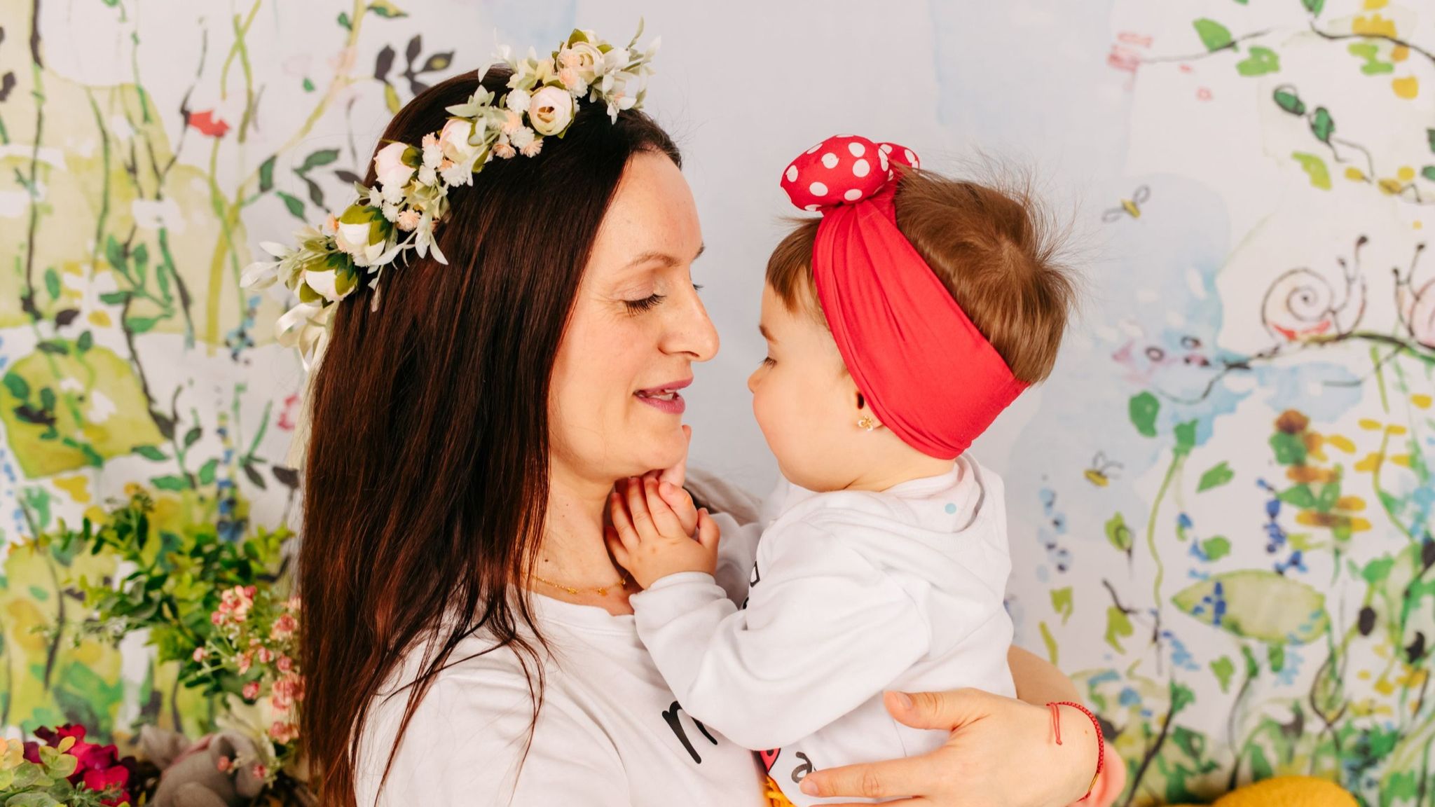 Mamă care își ține fetița în brațe pe covor, amândouă zâmbind și conectate emoțional într-o dimineață liniștită.