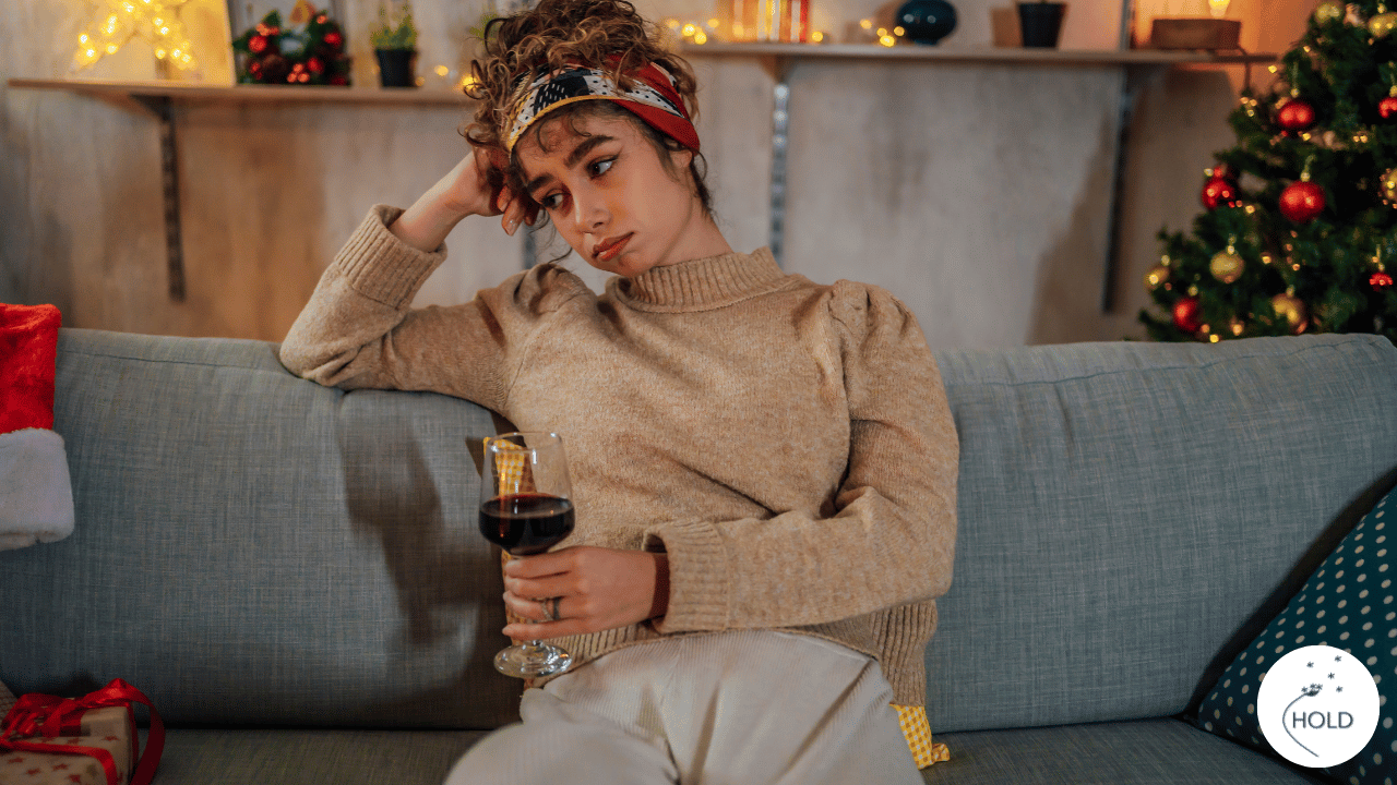 Overwhelmed woman sitting in a quiet room during the holidays, wishing for relief and emotional clarity, holding a glass of wine.