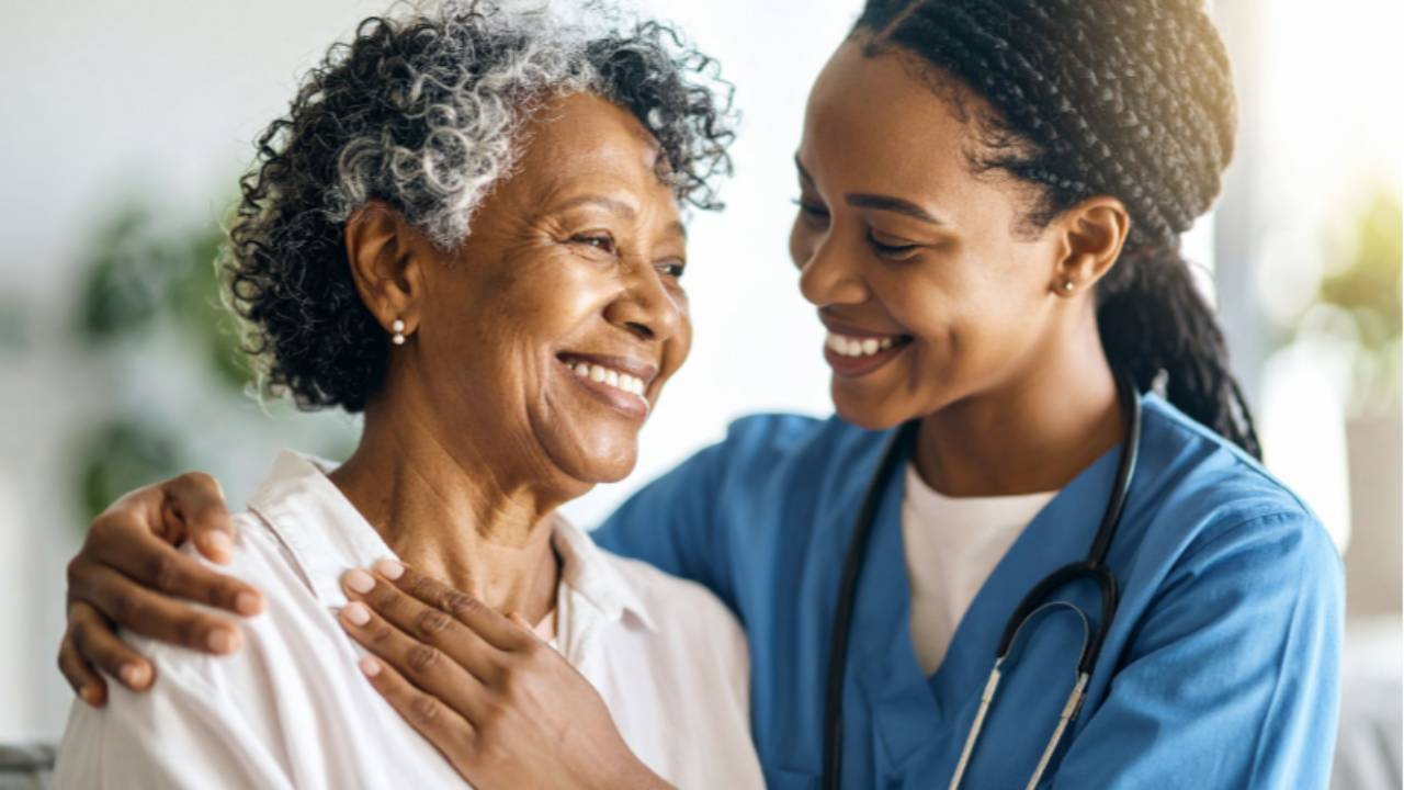 Smiling healthcare professional embracing an older woman, showing warmth and compassion in a caregiving setting.