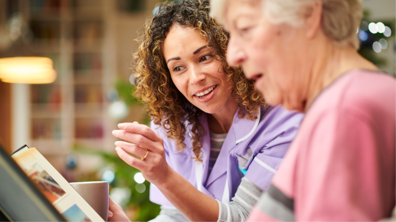 A caregiver smiling and talking with an elderly woman while looking at a photo album together