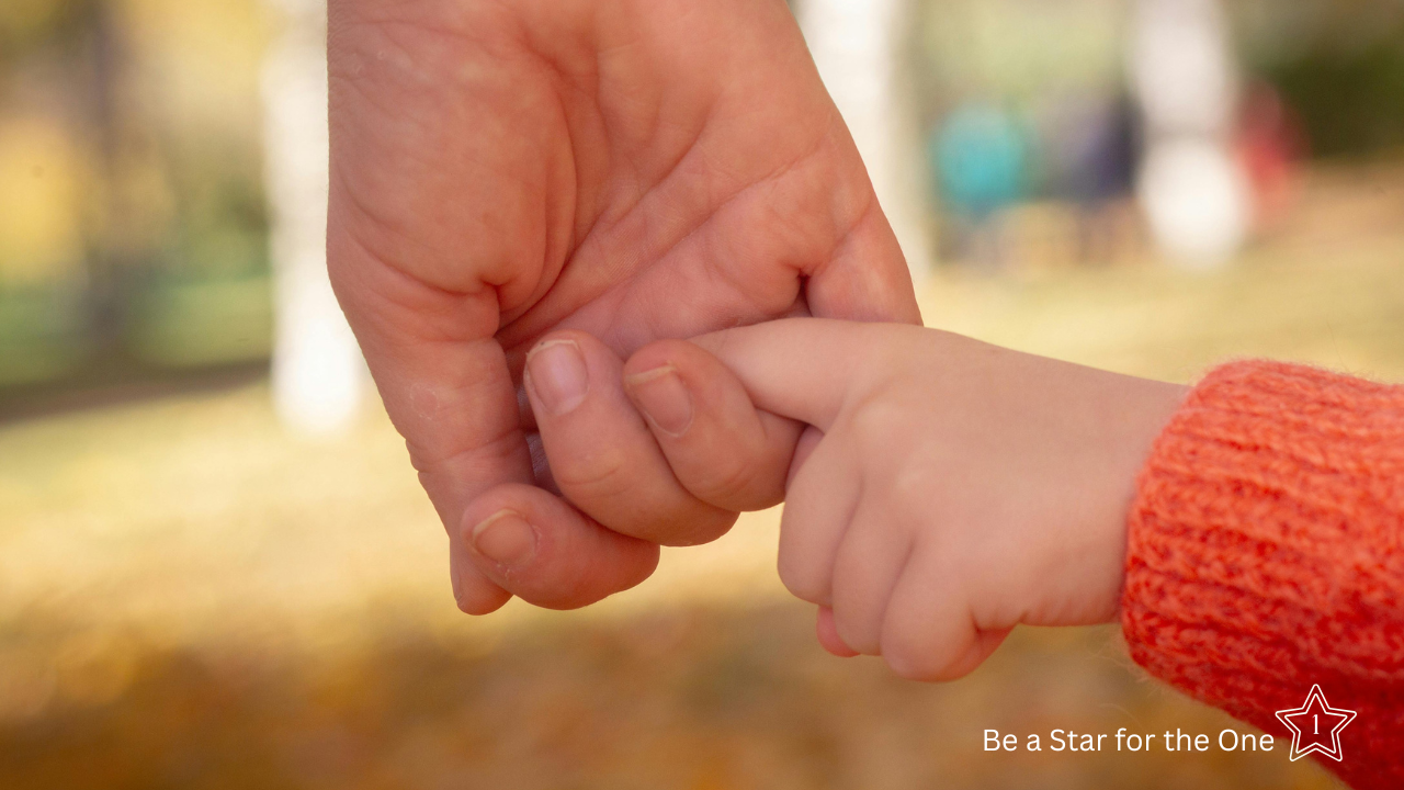 Close-up of an adult gently holding a child’s hand, representing compassion, protection, and hope for children facing hunger.