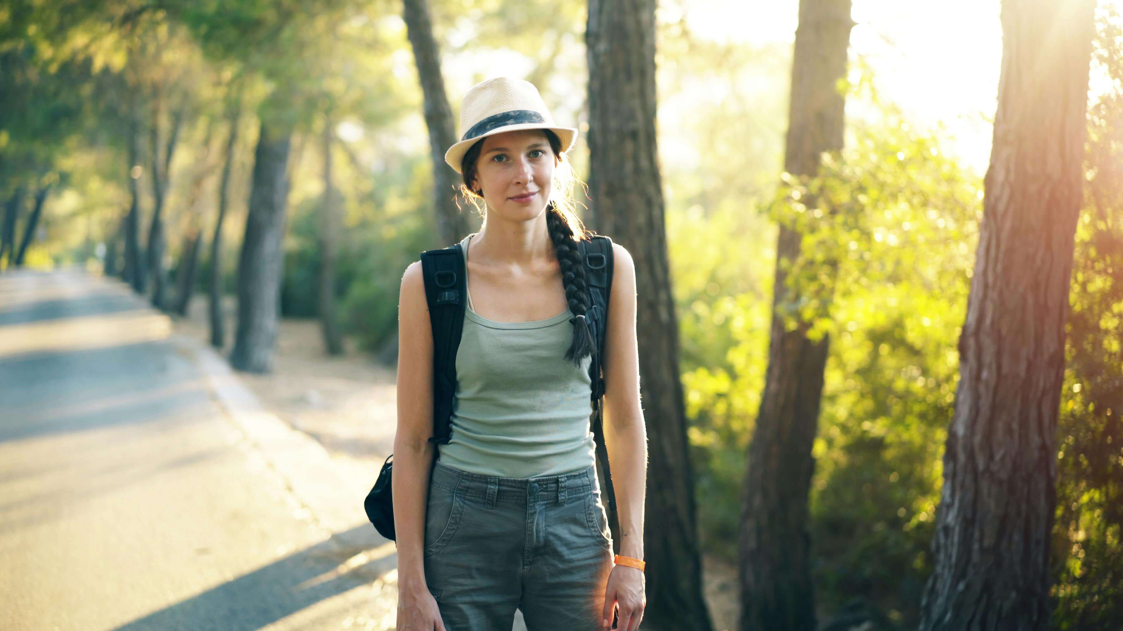 woman wearing a hat and backpack while standing on a sidewalk on a sunny day | international therapist | therapy for expats wanting roots | expat therapy online | Netherlands | England | France