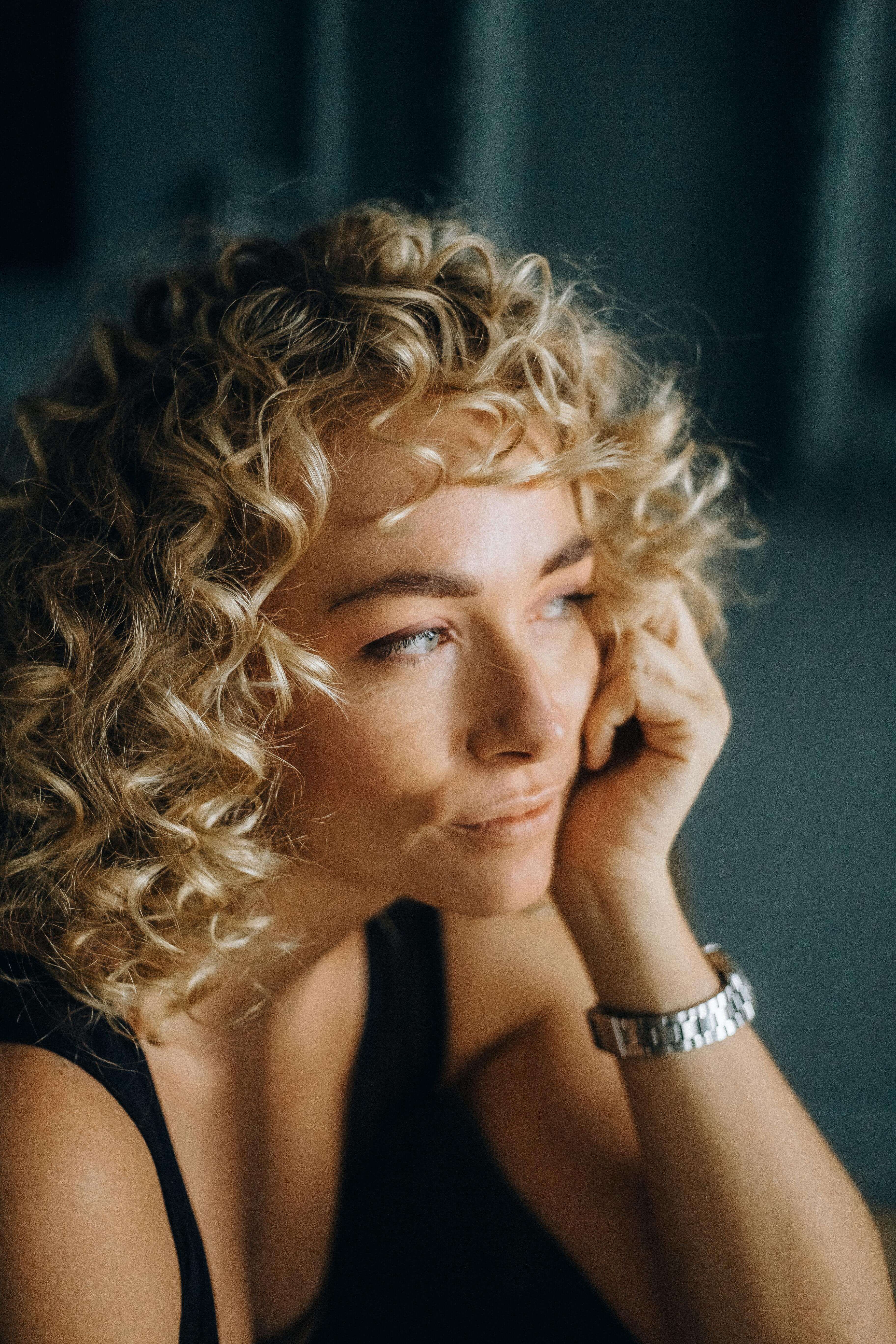 Close up of a curly haired woman resting her chin on hand looking pensively into the distance | expat belonging | who am i as a nomad identity | international therapist | scotland | canada | france