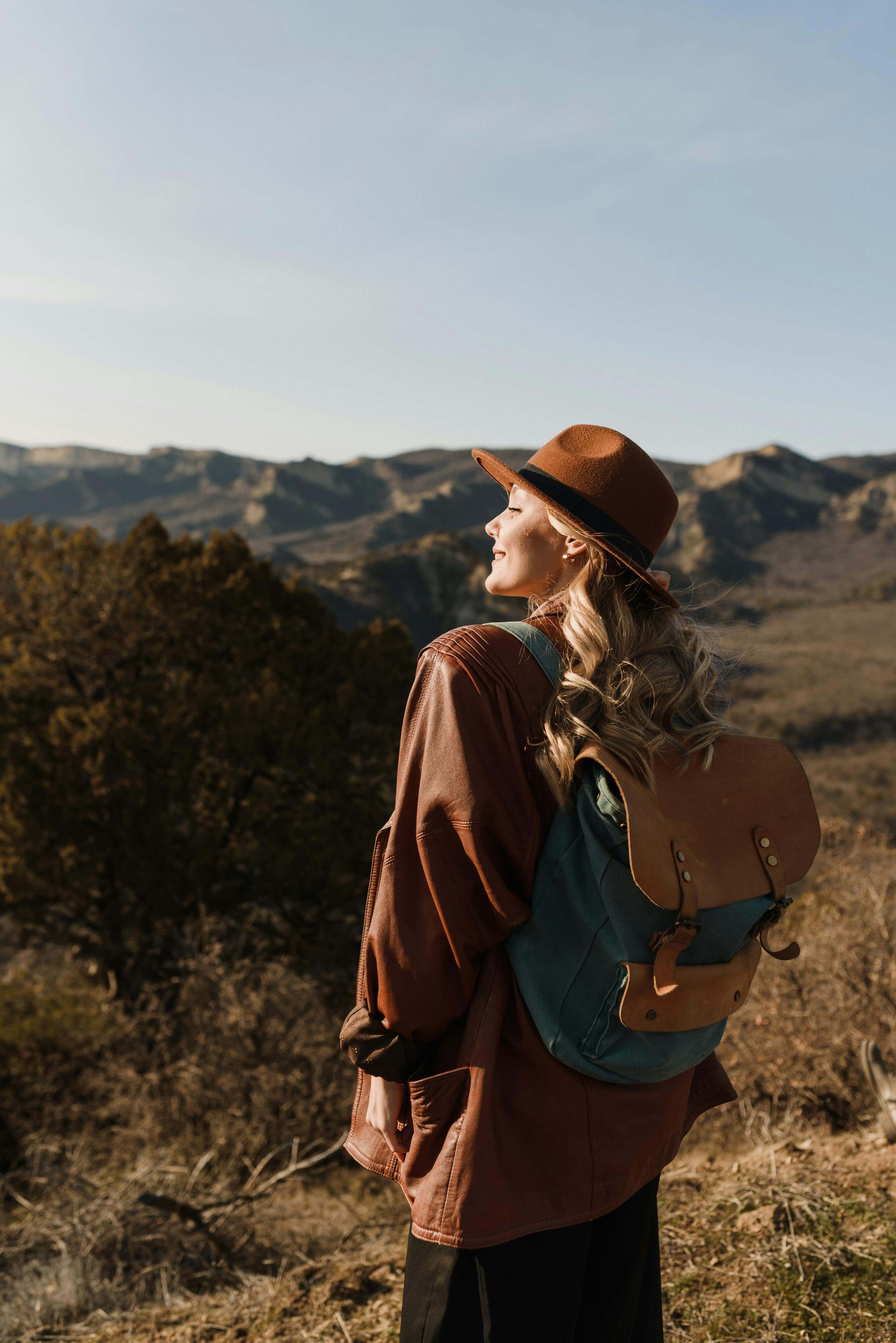 woman with leather backpack and wide brim hat looking out over a mountain landscape | love avoidance expat | international therapy and coaching | Scotland | Canada