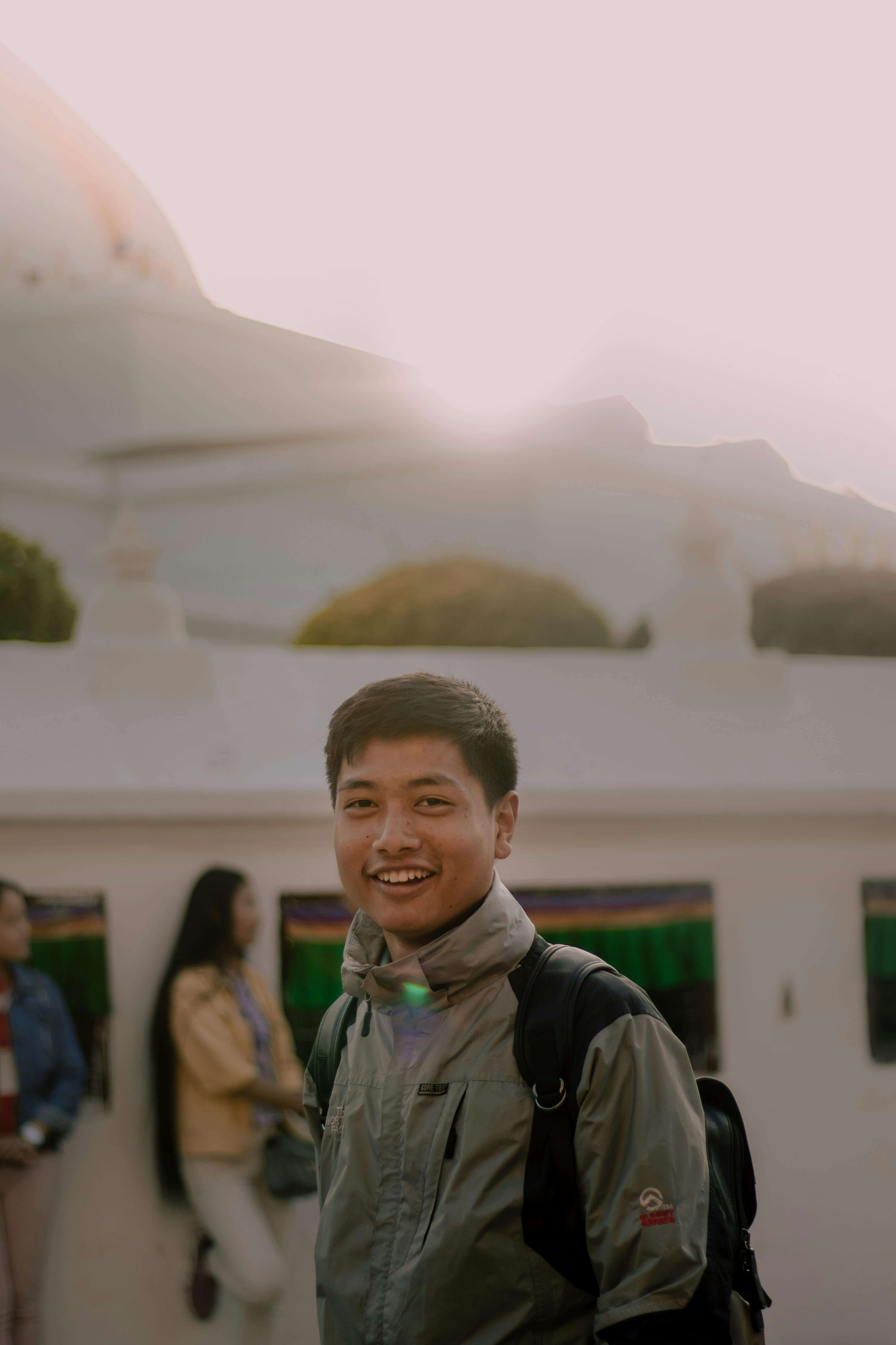 Smiling young man with a backpack standing in front of a white building in soft golden light | therapy for expats | always on edge expat | hypervigilance abroad | Scotland | Canada | France