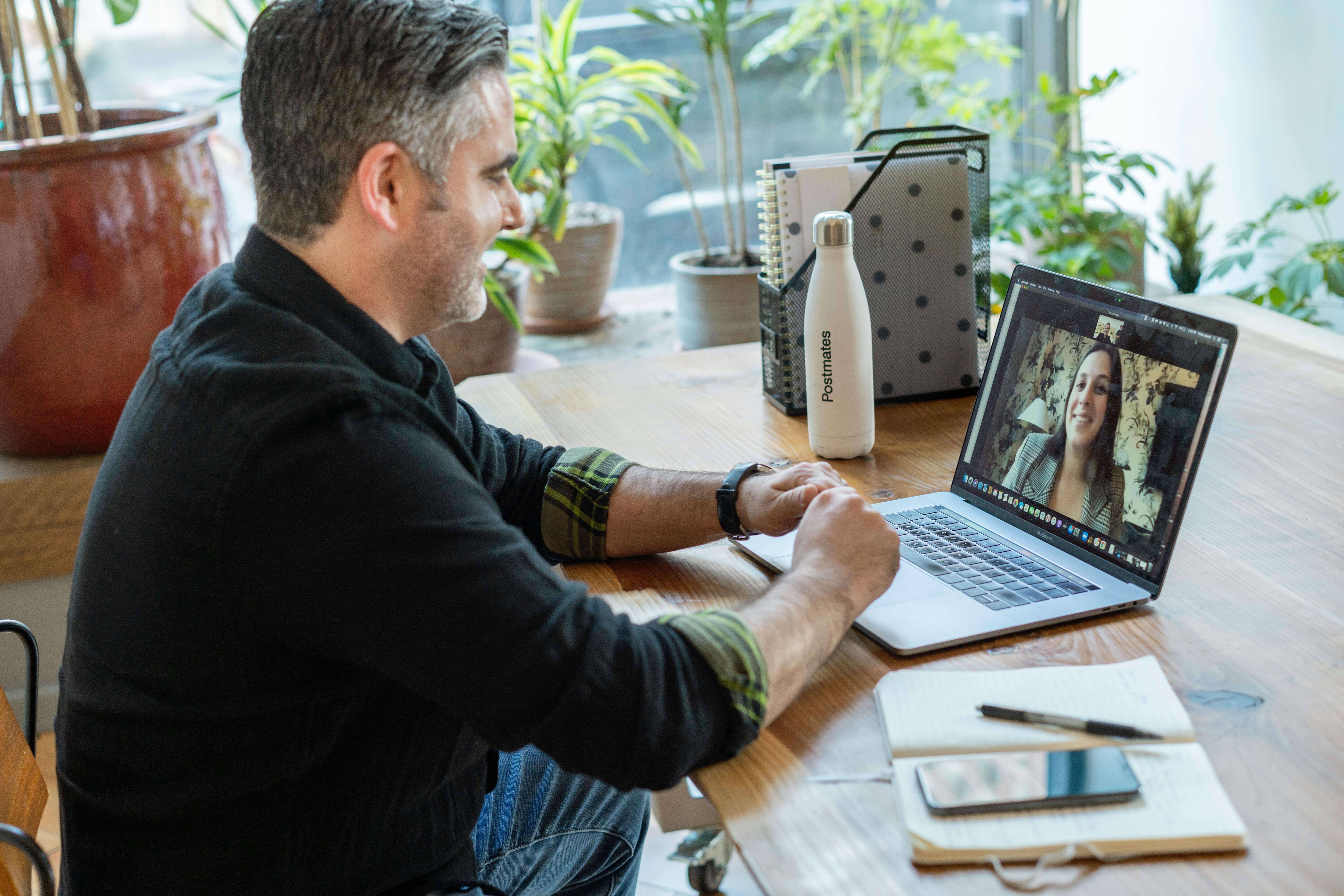 Man sitting at a desk with plants in the background on a video call with a woman on his laptop | international therapy and coaching | international therapist | online therapy for expats | United States | South Africa