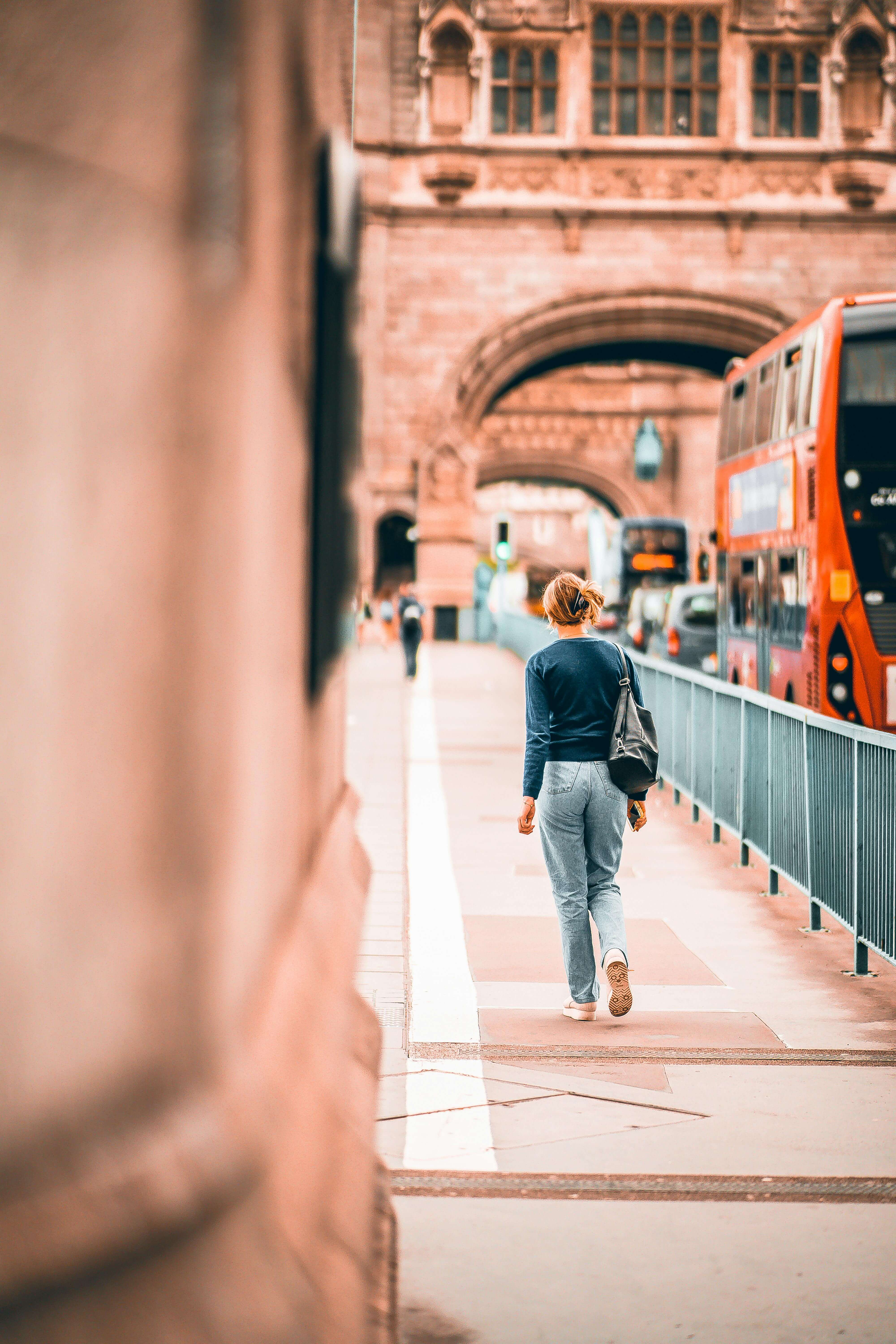 Woman walking away from camera across Tower Bridge in London with a red double decker bus beside her | international therapy and coaching | international therapist | living abroad mental health | England | Italy | Germany
