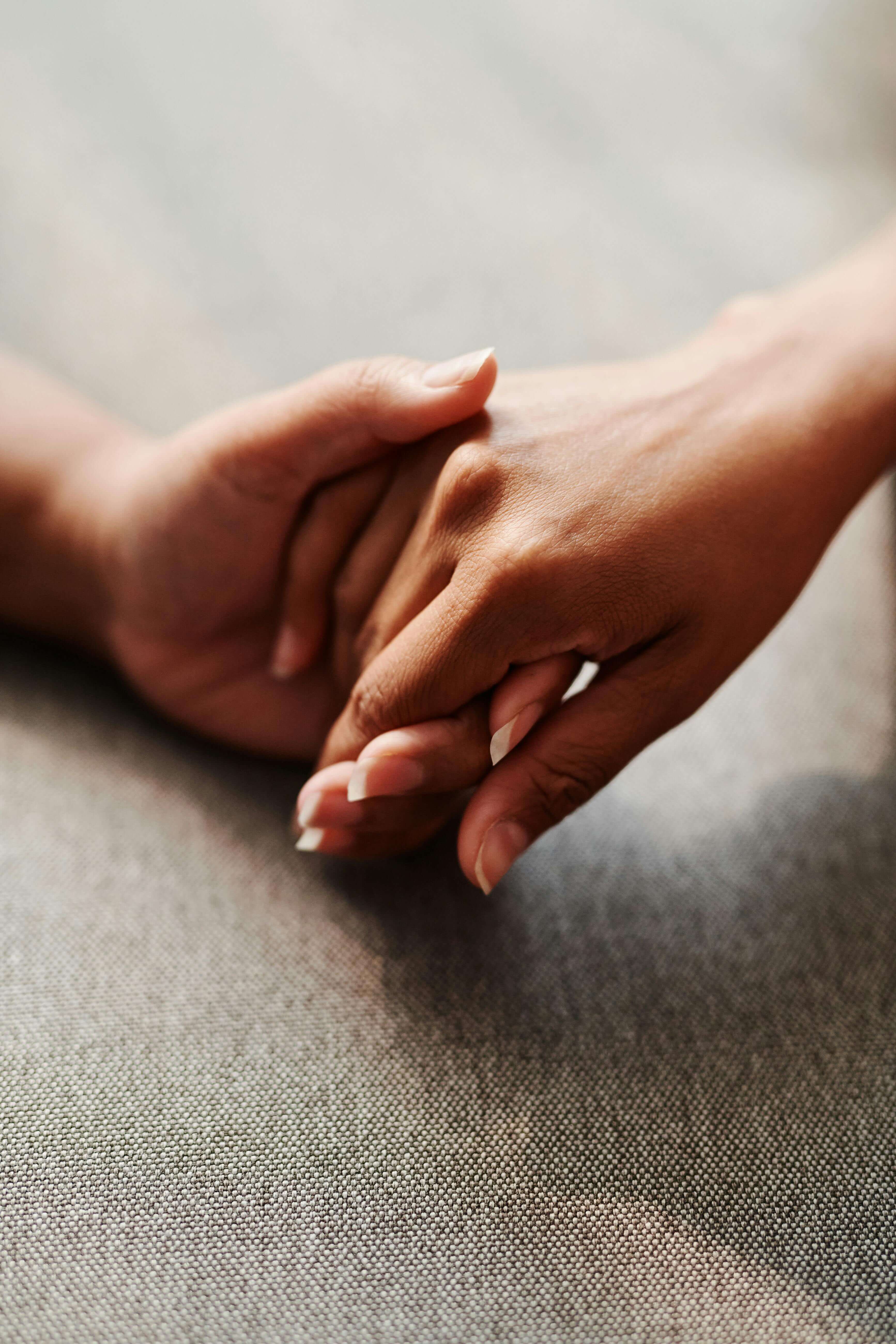 Close up of two people holding hands gently on a grey fabric surface | expat fear of commitment | international therapy and coaching | expat commitment issues | Germany | Portugal | Italy