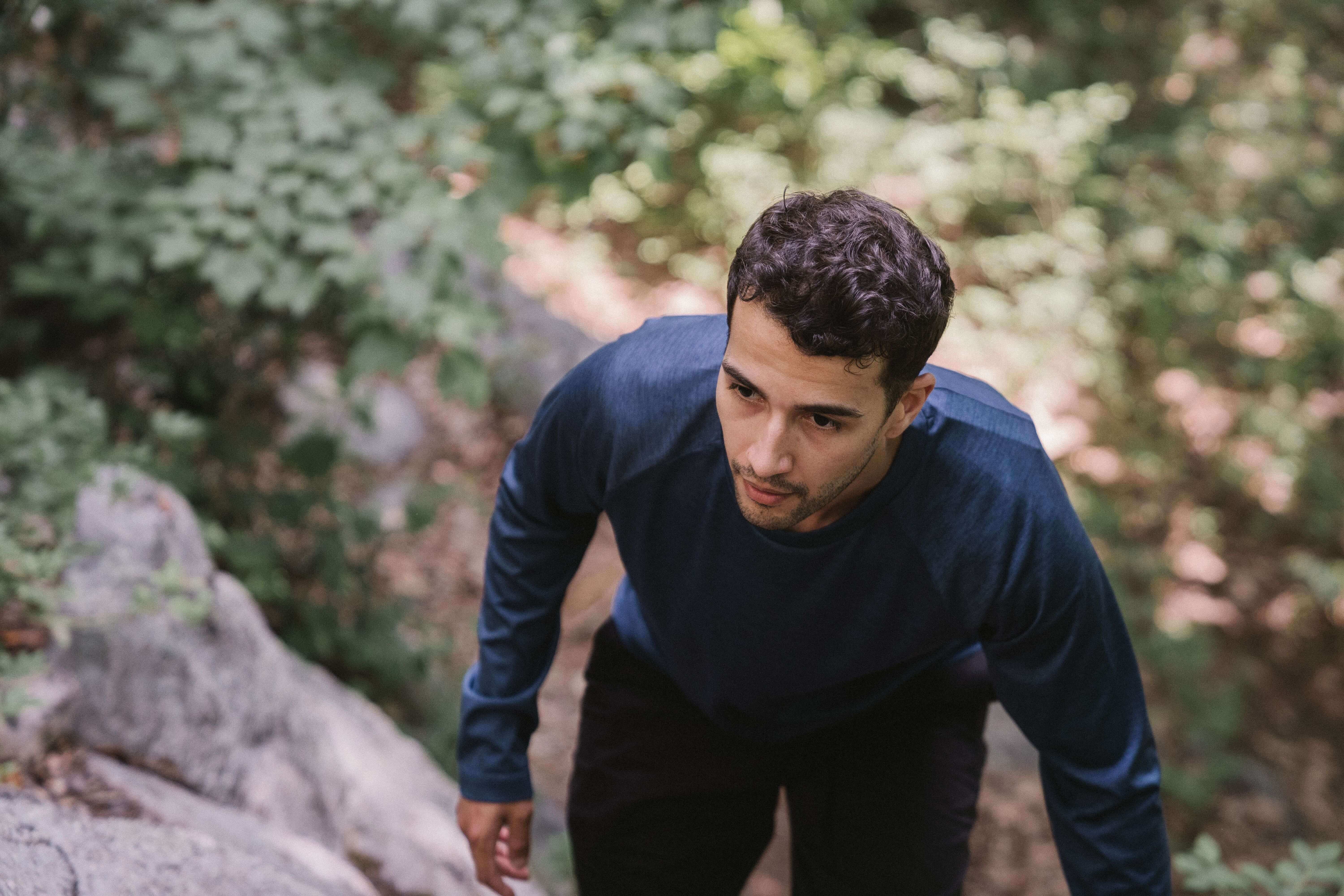 Young man in a navy long sleeve shirt climbing rocky terrain in a lush green forest with a focused determined expression | executive coaching | international trauma therapist | therapeutic coaching | Chicago | Los Angeles | Seattle