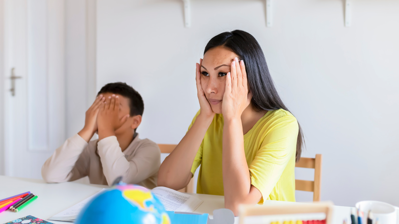 Overwhelmed parent sitting at table with child during stressful moment at home