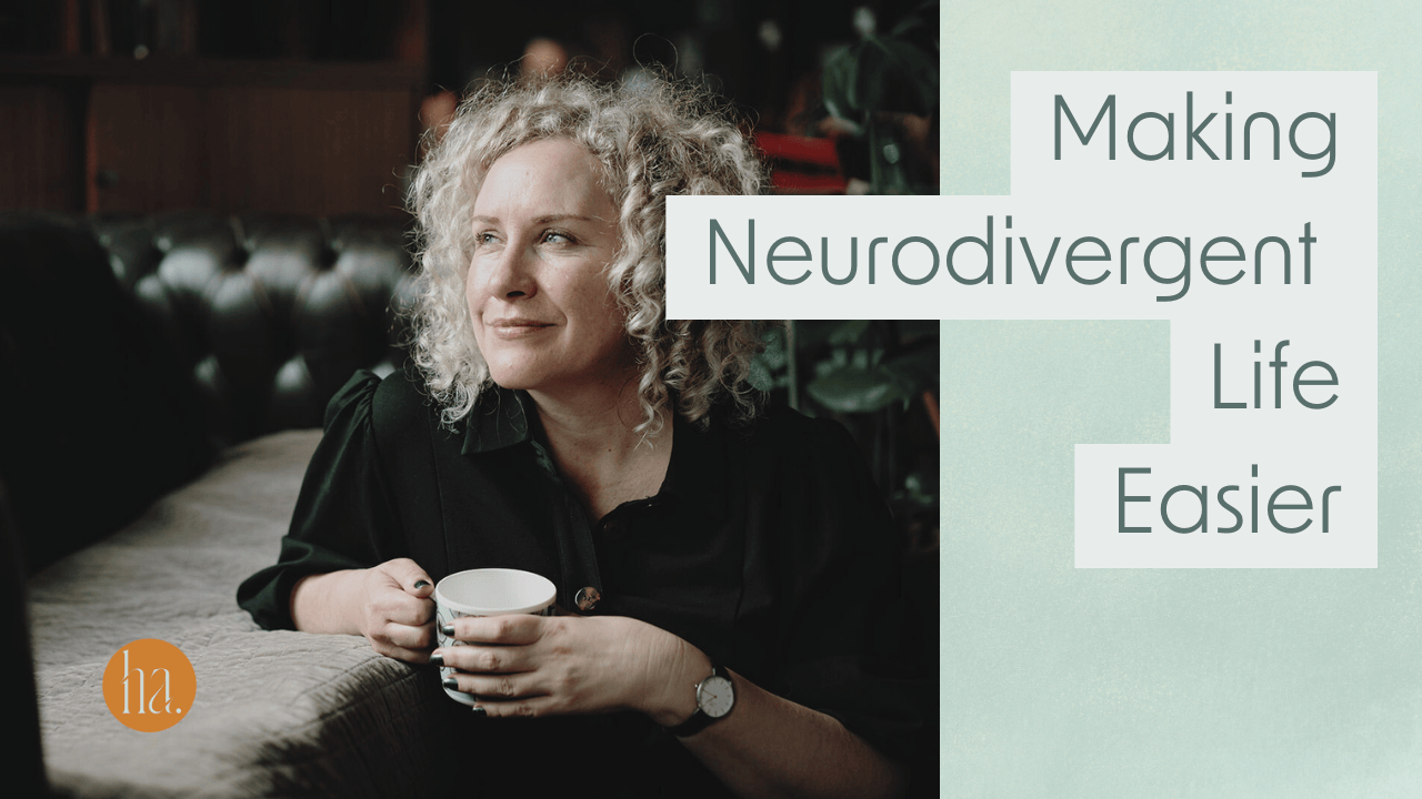 A neurodiverse woman with curly hair wearing a black jumpsuit holds a cup of tea sitting next to a Chesterfield sofa while she ponders how to make her life easier.