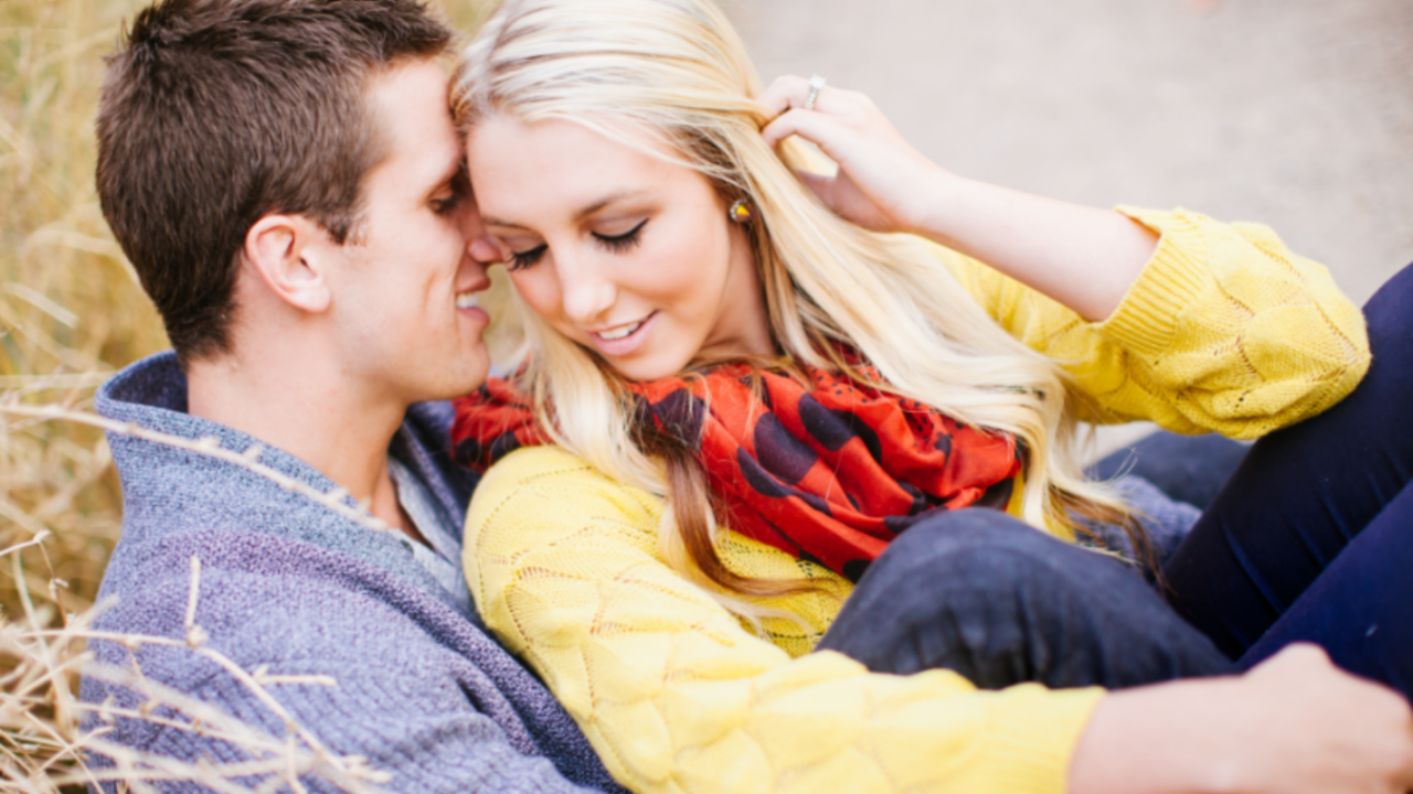 Newlywed couple sitting closely together outdoors, smiling softly and leaning into each other, capturing a tender and joyful moment that reflects the intimacy and connection of a honeymoon for LDS couples.
