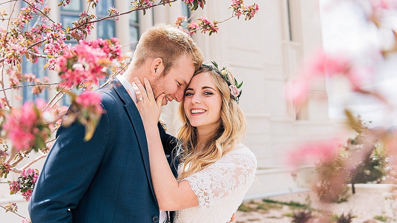 LDS Bride and groom surrounded by blooming pink spring blossoms outside the Payson Utah Temple, captured by Kylee Ann Photography.