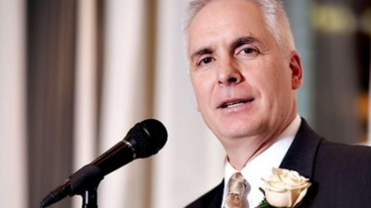 Man giving a heartfelt wedding toast at a reception with microphone, wearing a suit and boutonniere, symbolizing meaningful wedding speeches
