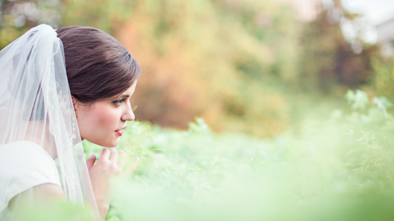Pensive LDS bride in a modest wedding dress in a beautiful natural setting, wondering why brides toss bouquets and other wedding traditions.