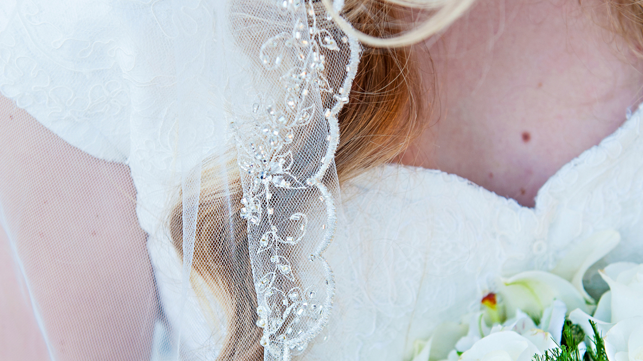Close-up of modest lace wedding dress with delicate sleeve detail and soft bridal bouquet, showing elegant modest design
