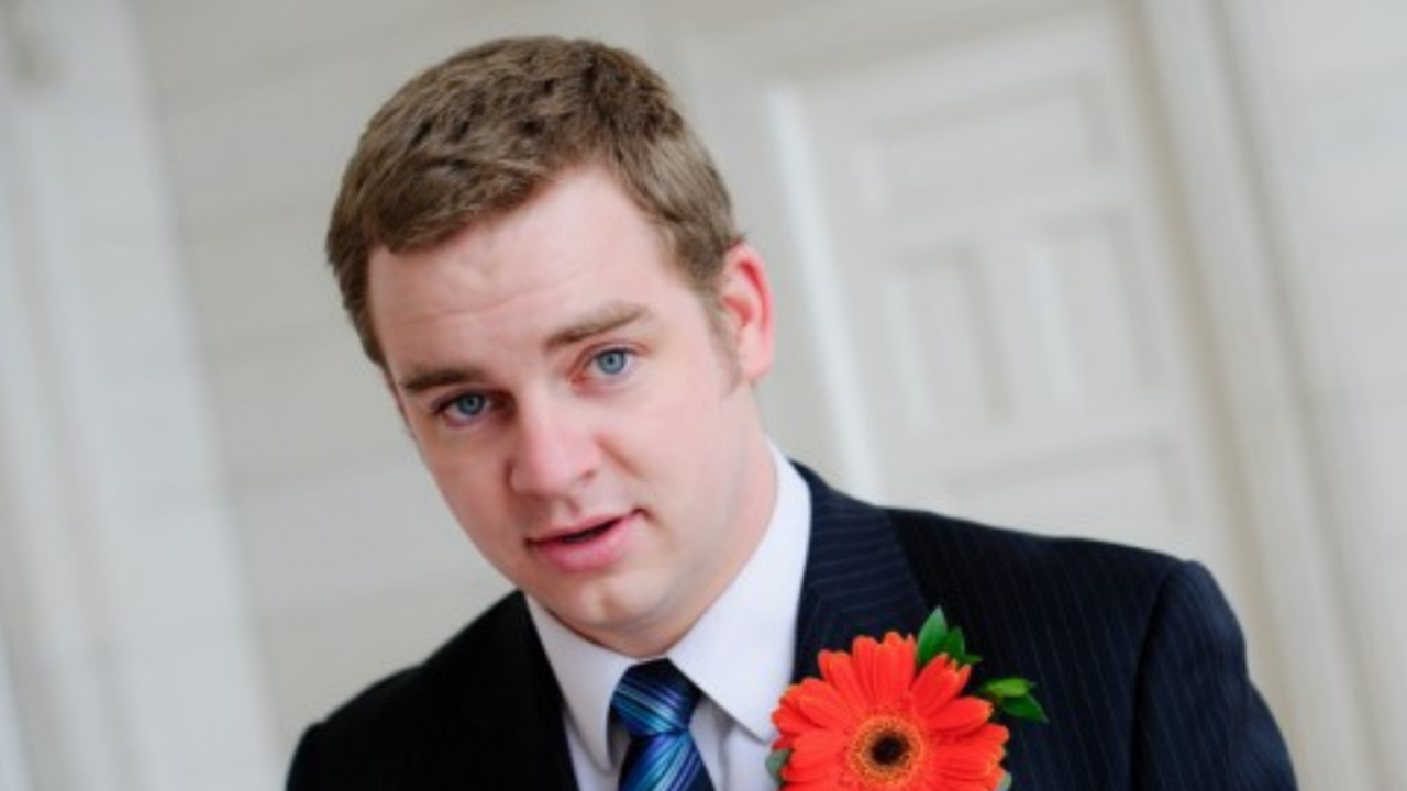 Man in suit with boutonniere preparing to give a wedding speech, symbolizing overcoming public speaking anxiety at a reception.