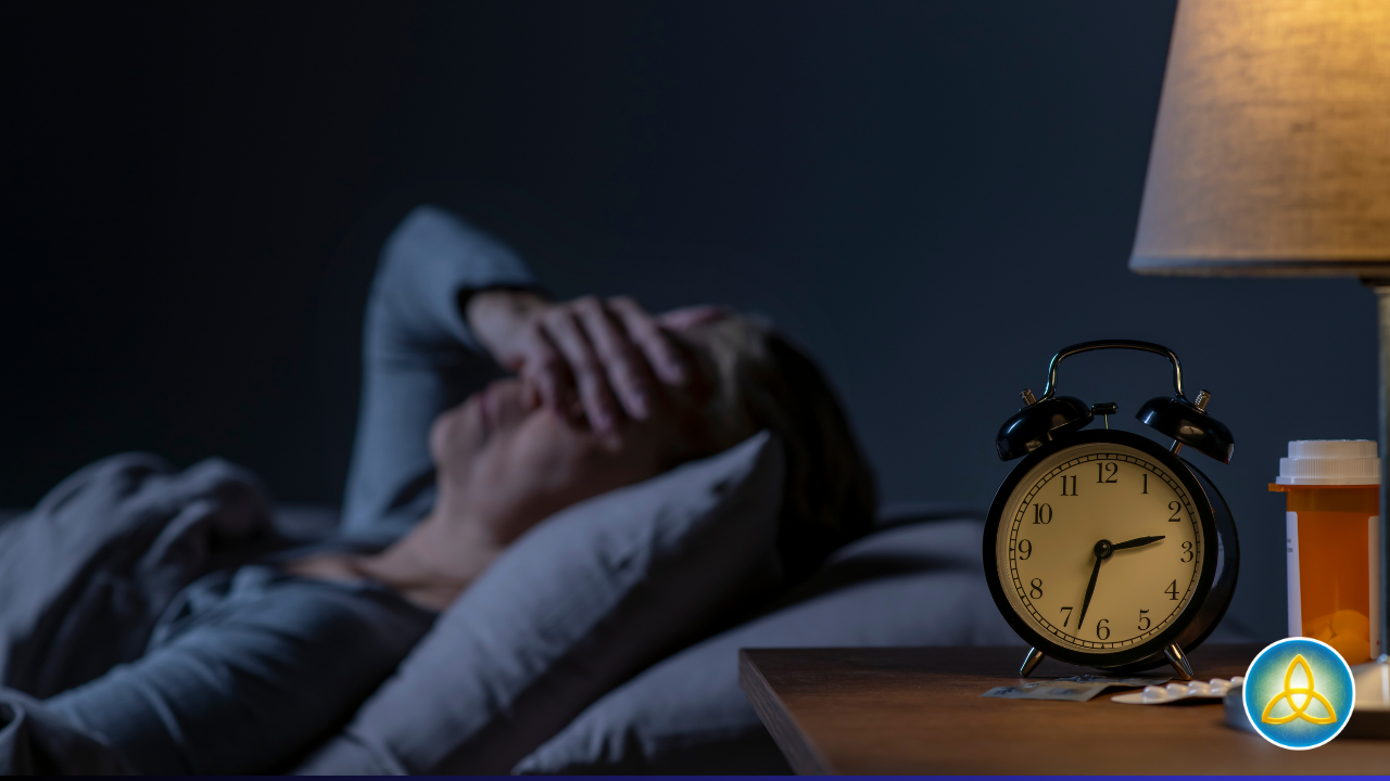 Person lying awake in bed at night with hand over face, alarm clock showing early morning hours, illustrating insomnia and racing thoughts.
