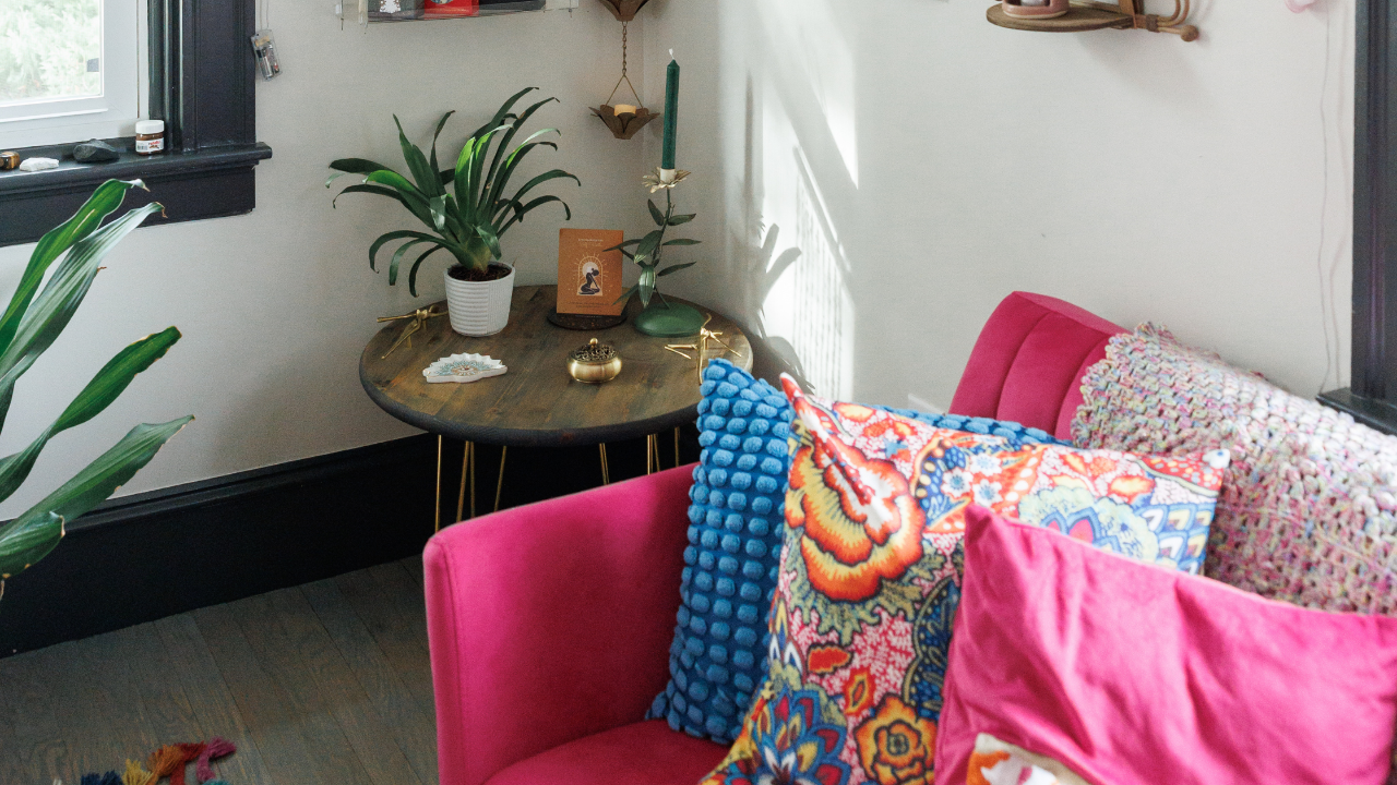 Vibrant pink velvet armchair in a sunny living room with patterned pillows and a small wooden side table.