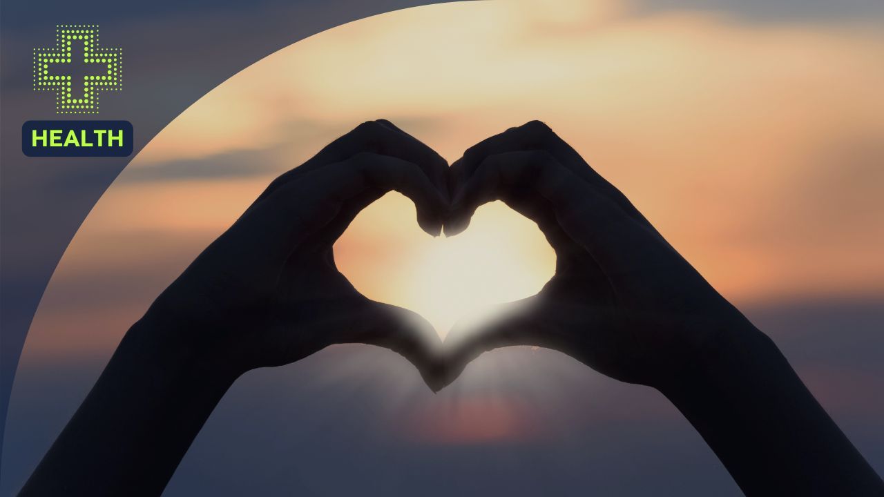Hands forming a heart shape around the sun during a sunset, symbolizing self-love, wellness, and emotional well-being.