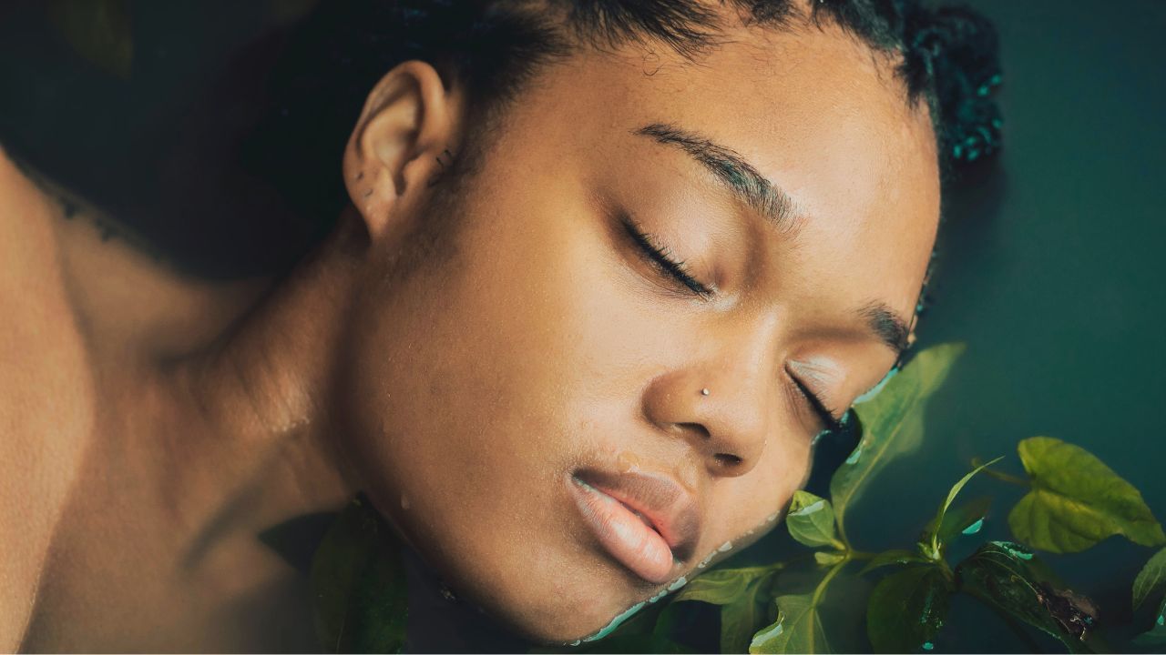 A woman with large braids of black hair stands in a lake. She appears relaxed, calm, and at one with nature.