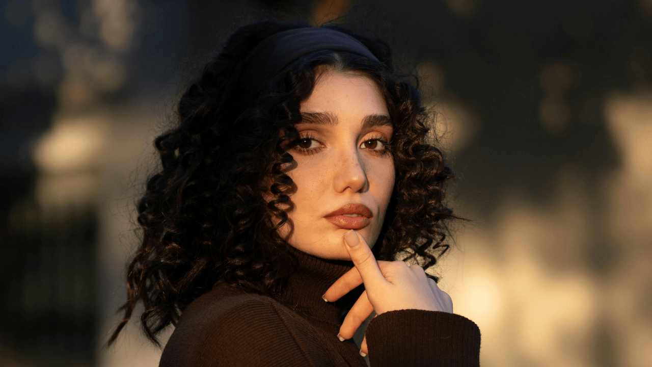A woman with curly dark hair is looking at the camera. She looks bold, audacious and self-confident.