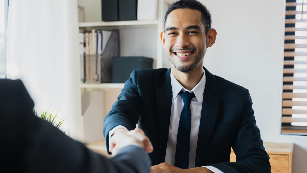 A man smiling, shaking hands with a client or coworker, showing how men are their best selves at work.