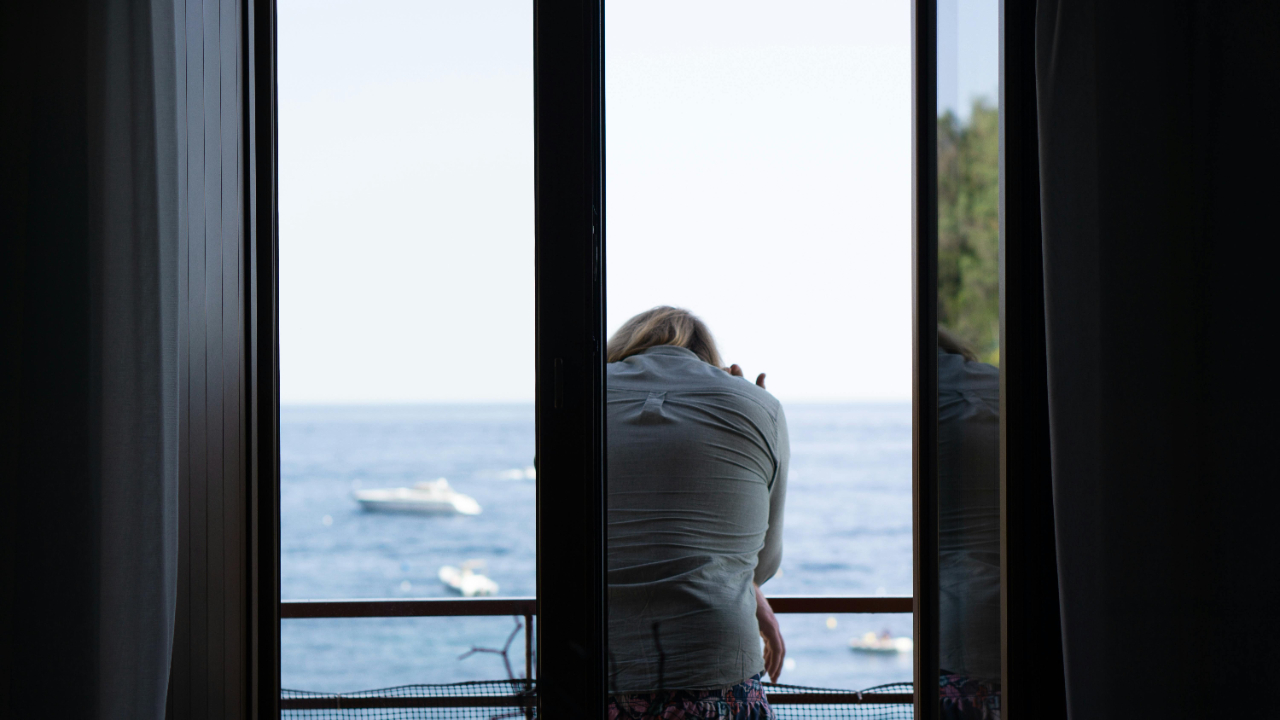 View of woman from behind leaning on a balcony. She seems unhappy or maybe distressed.