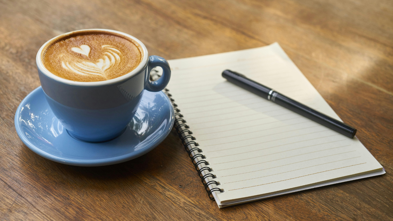 A latte coffee next to a pen and open notebook on a table, ready for a moment of reflection on the past year.