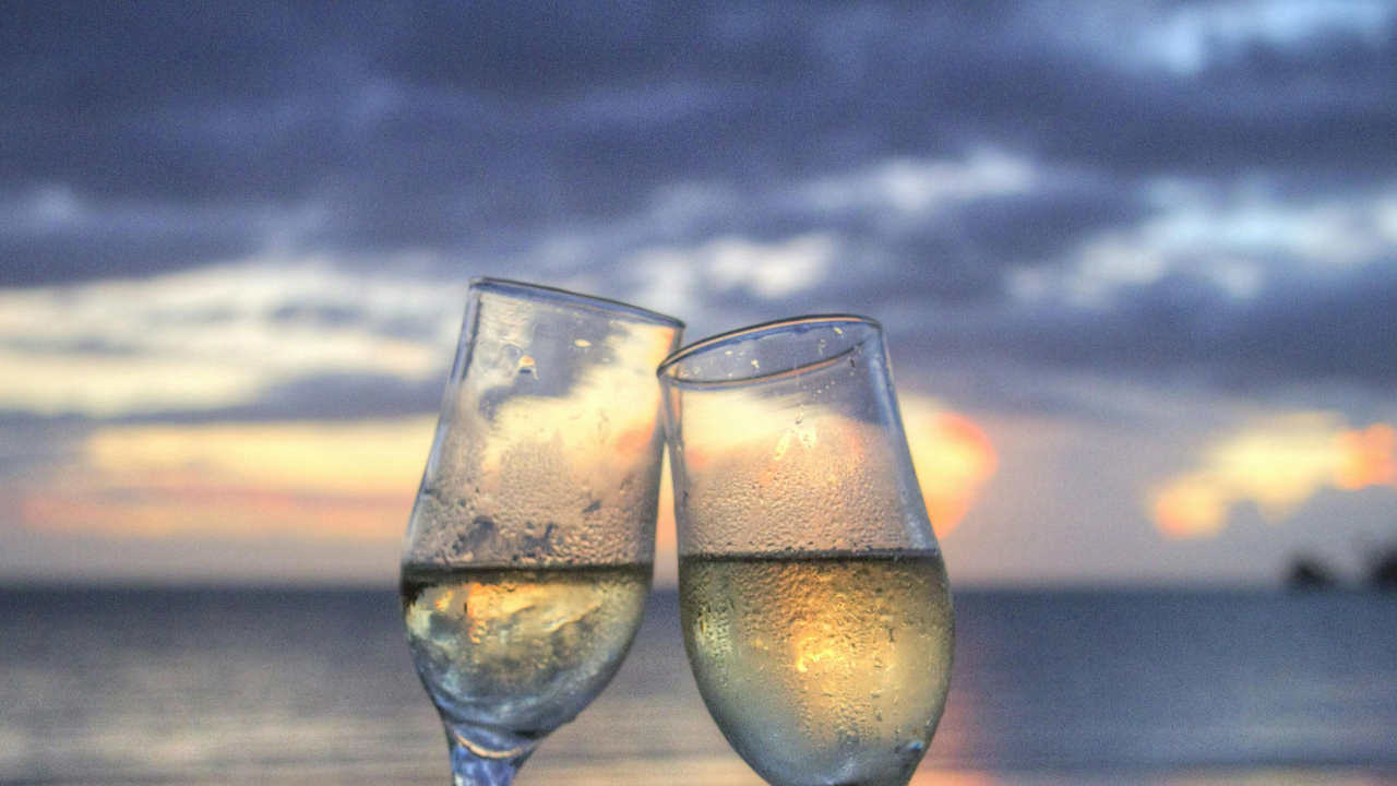 Two glasses clinking at sunset on a beach, symbolizing romance and connection in marriage.