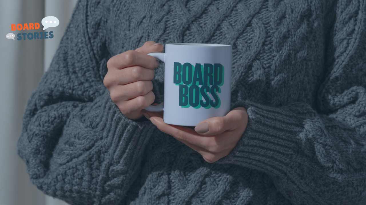 An close up image of a person in a blue knit sweater holding a mug in their hands that reads 'Board Boss'.